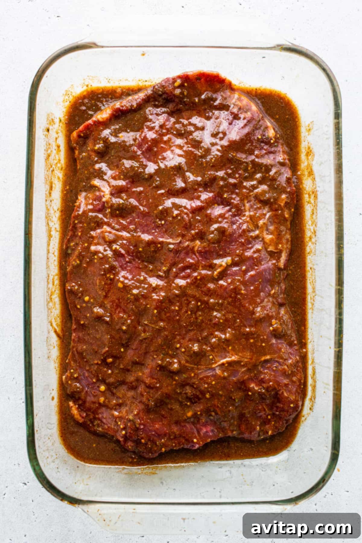 Flank Steak Marinating for Fajitas Flank steak fully submerged in the vibrant fajita marinade within a glass baking dish, ready for refrigeration.