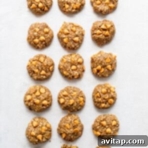Uniform cookie dough balls, gently flattened, lined up on a baking sheet, ready for the oven.