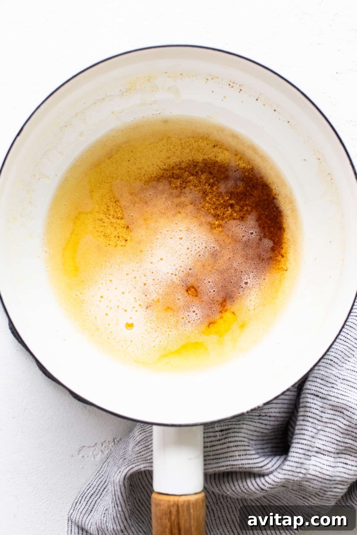 Close-up photo of unsalted butter browning in a small saucepan on the stove, showing amber color and milk solids.