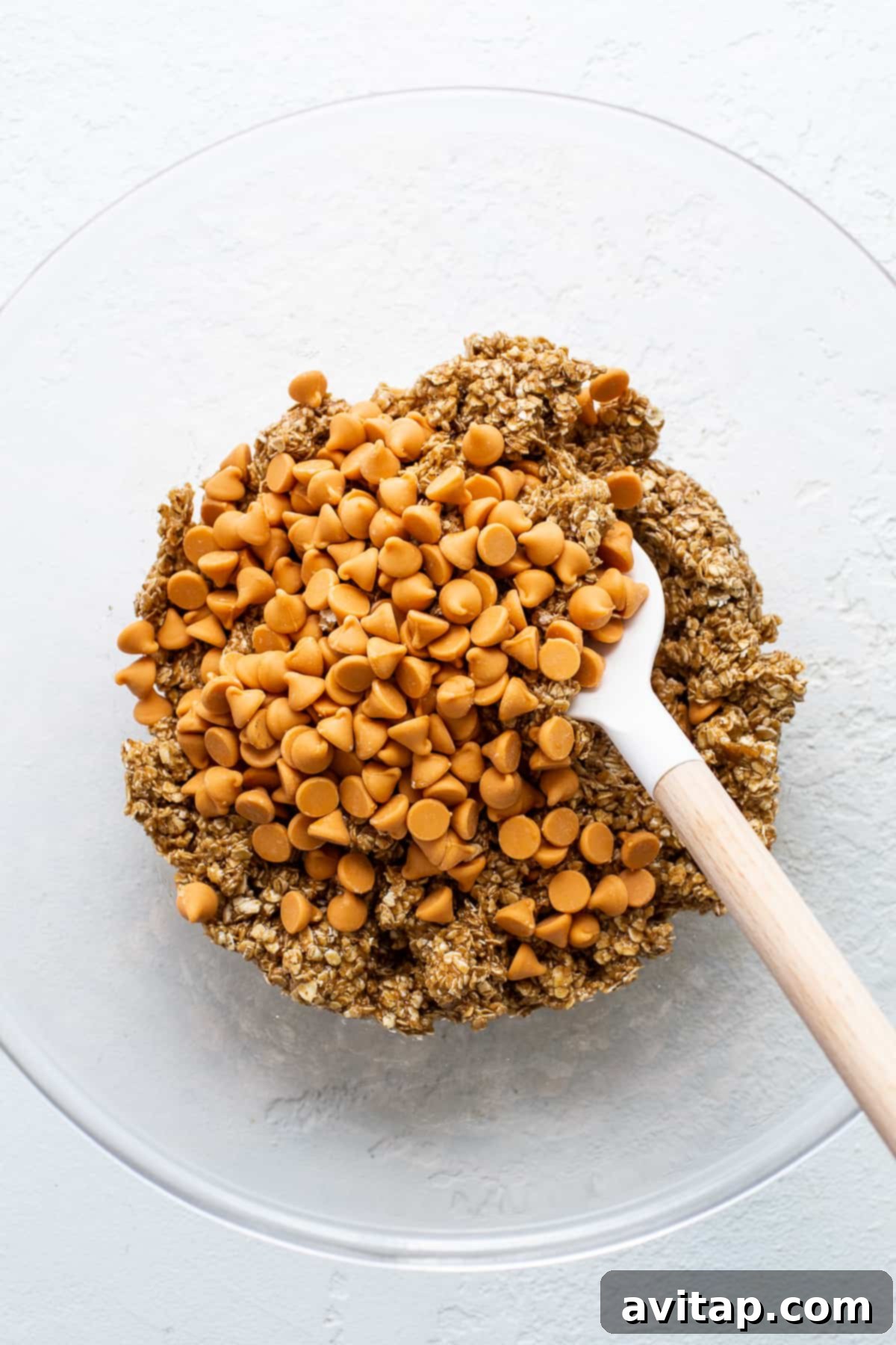 Ingredients for flourless brown butter oatmeal butterscotch cookies in a mixing bowl before combining, showing oats, chips, and wet mixture.