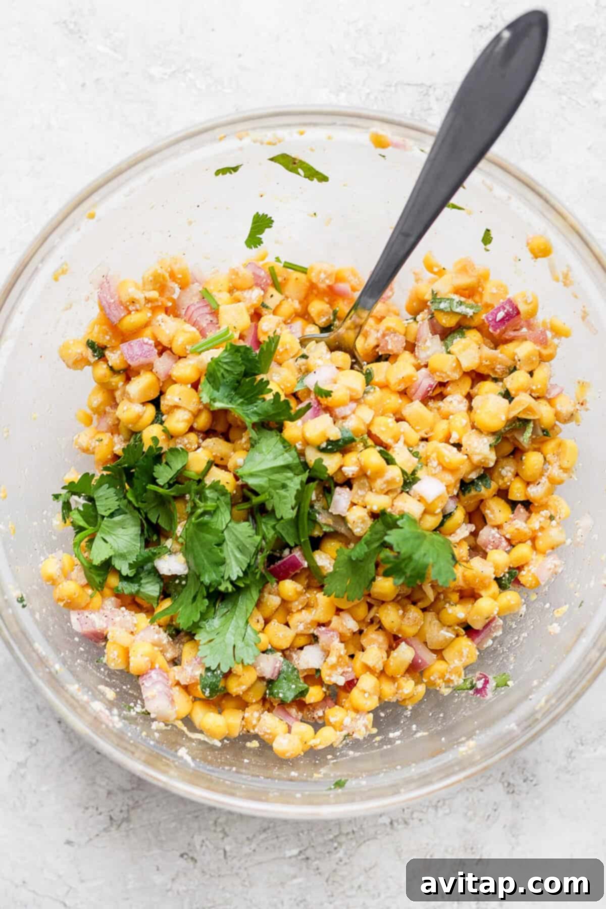 A glass bowl filled with a delightful Mexican street corn salad and slow cooker carnitas.