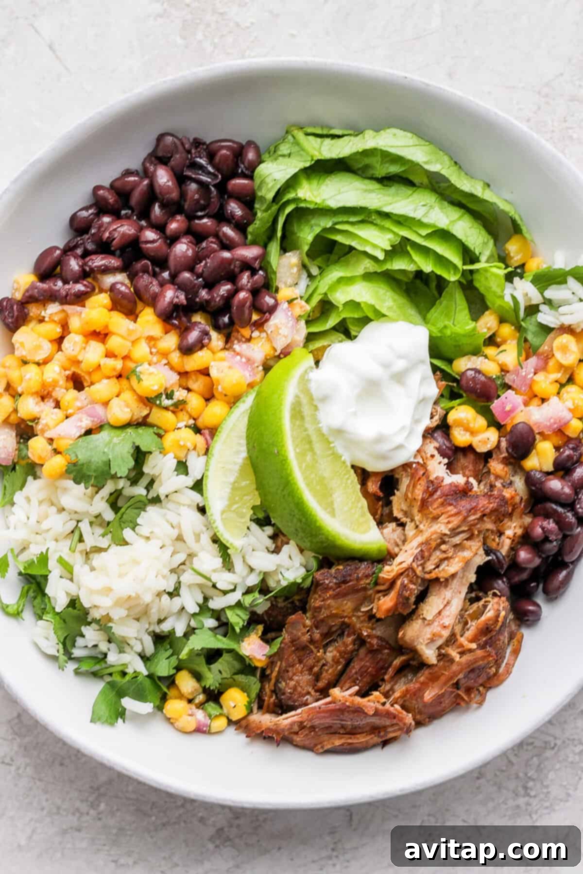 A hearty bowl of slow cooker carnitas salad, layered with corn, beans, and a dollop of sour cream.