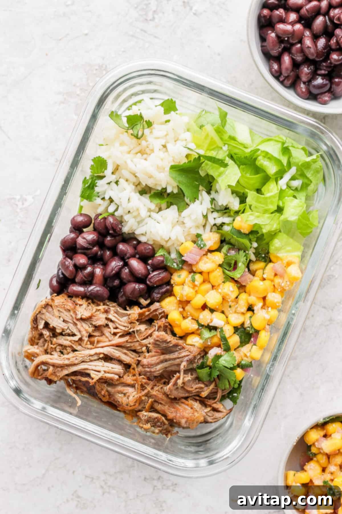 A perfectly prepared slow cooker carnitas meal with rice, beans, and corn, neatly packed in a glass container for meal prep.