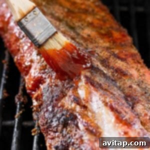 A barbecue grill with a spatula applying BBQ sauce to the ribs.