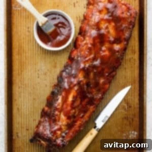 Cooked BBQ ribs on a tray with a knife and a side of ketchup.