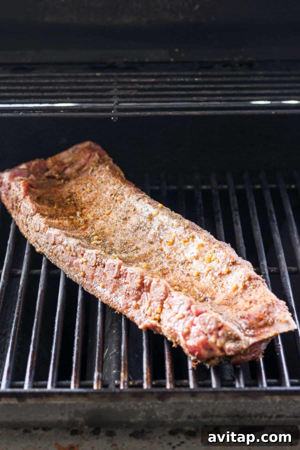 A full rack of baby back ribs sizzling on a hot grill, charring beautifully.
