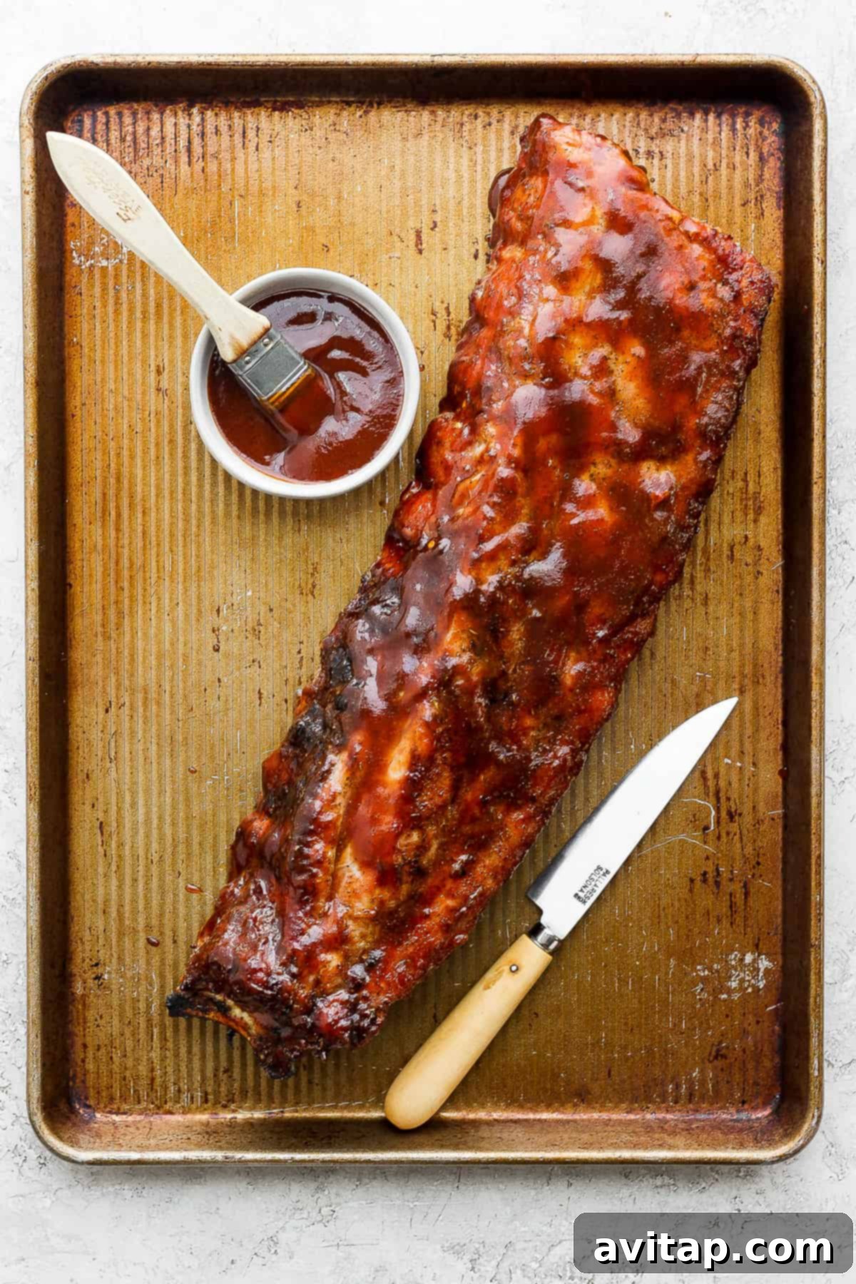 Grilled ribs cooling on a baking sheet before being cut, showcasing their beautiful char and color.
