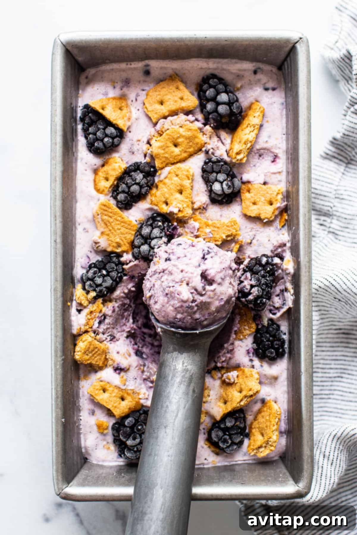 Scoops of high-protein blackberry cheesecake cottage cheese ice cream in a bread pan, garnished with fresh blackberries and graham cracker crumbs.