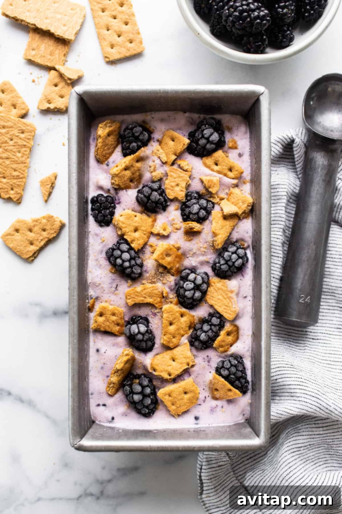 Blackberry cheesecake cottage cheese ice cream in a tin loaf pan, garnished with fresh berries and graham cracker crumbles.