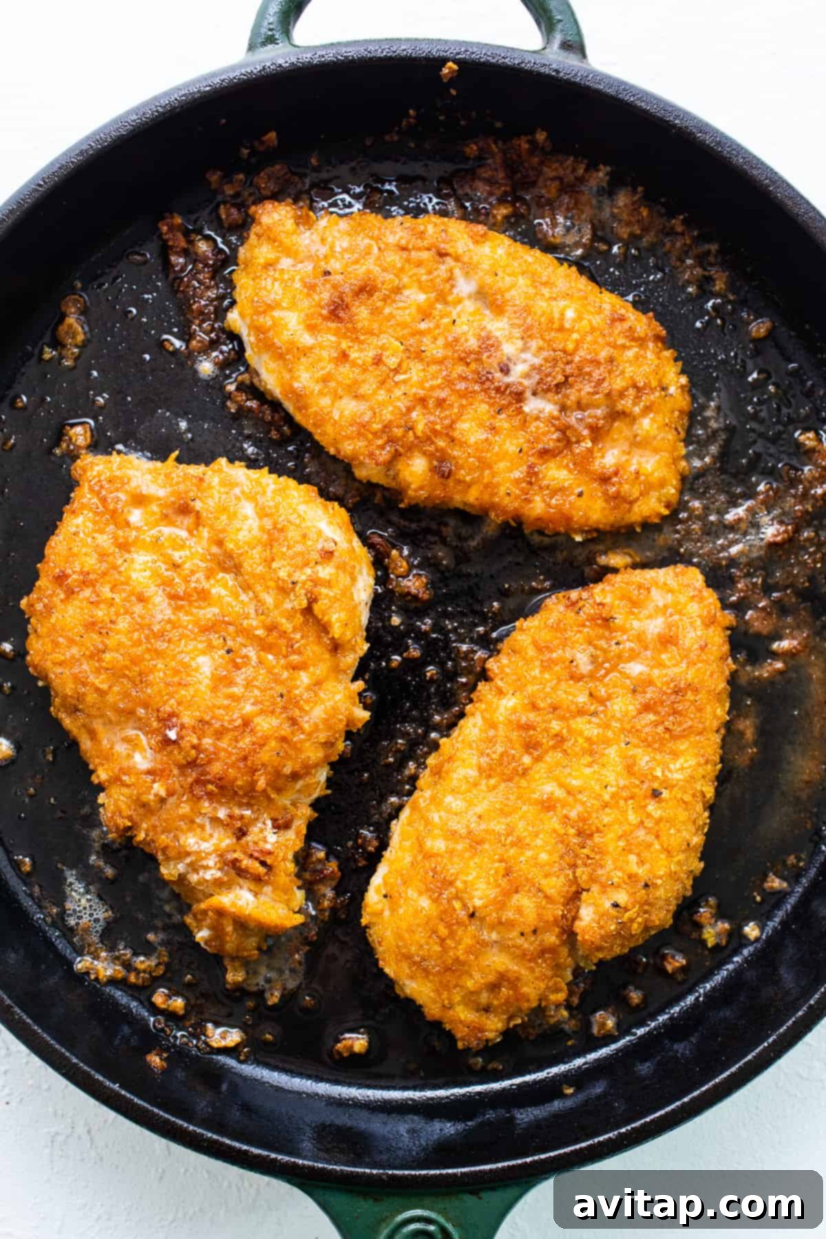 Crispy chicken breasts cooking in a cast iron pan, turning golden brown.