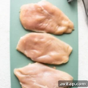 Chicken breast being pounded on a cutting board to an even thickness.