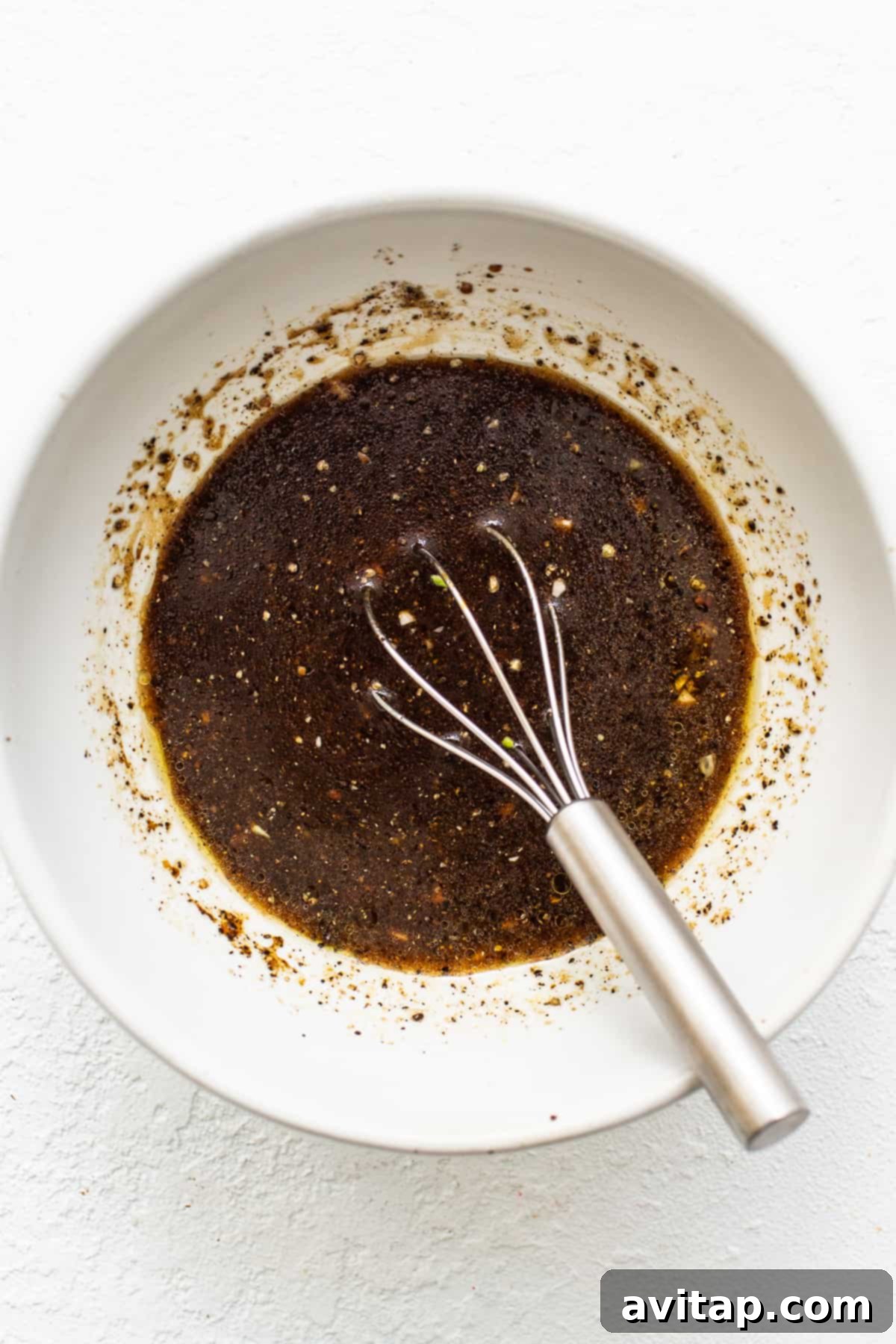A collection of marinade ingredients, including liquids, spices, and fresh aromatics, whisked together in a bowl, ready to be used.