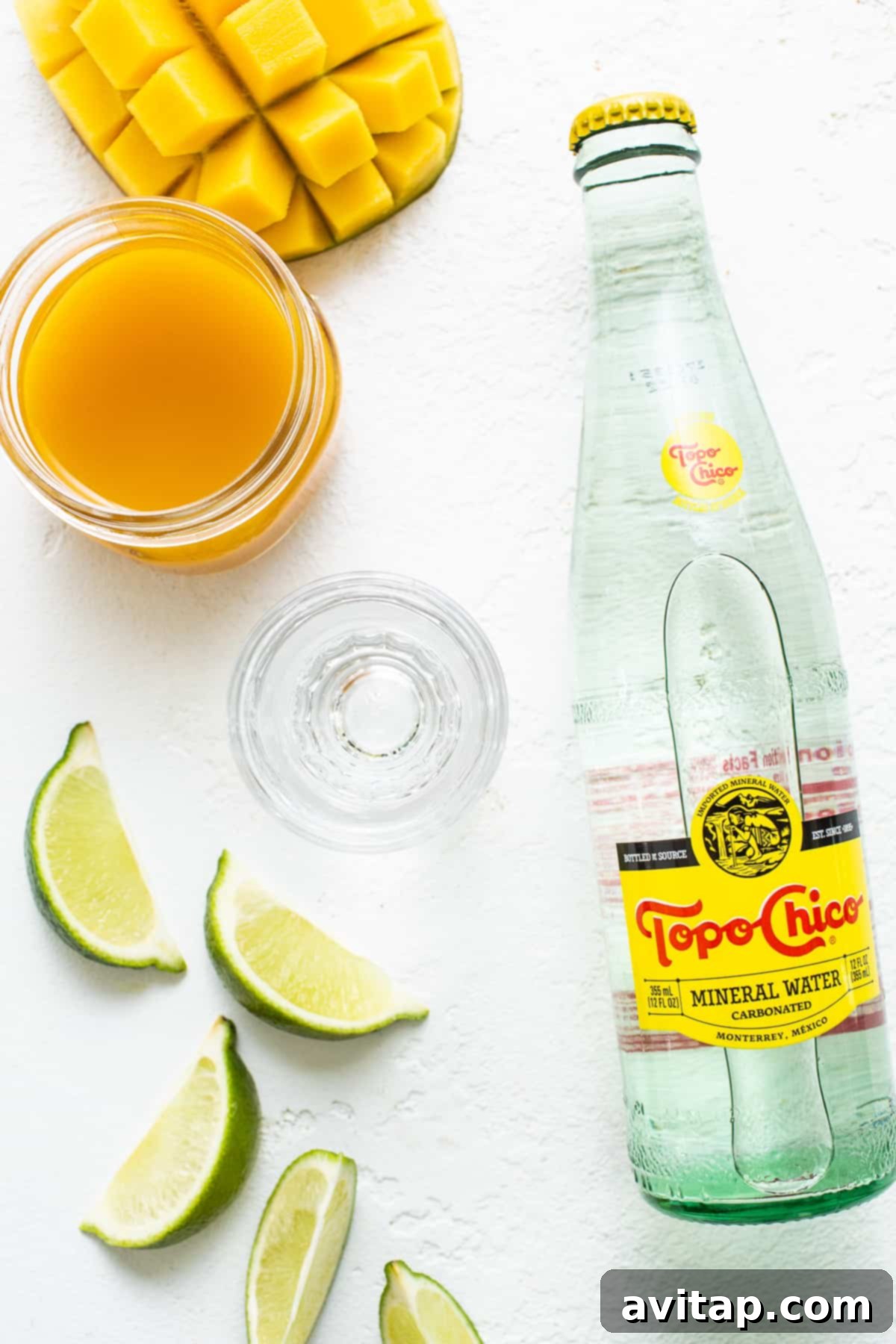 Ranch Water Ingredients: Tequila, Topo Chico, Fruit Juice, Lime Fresh ingredients laid out for making Ranch Water: Topo Chico bottles, tequila, various fruit juices, and limes.