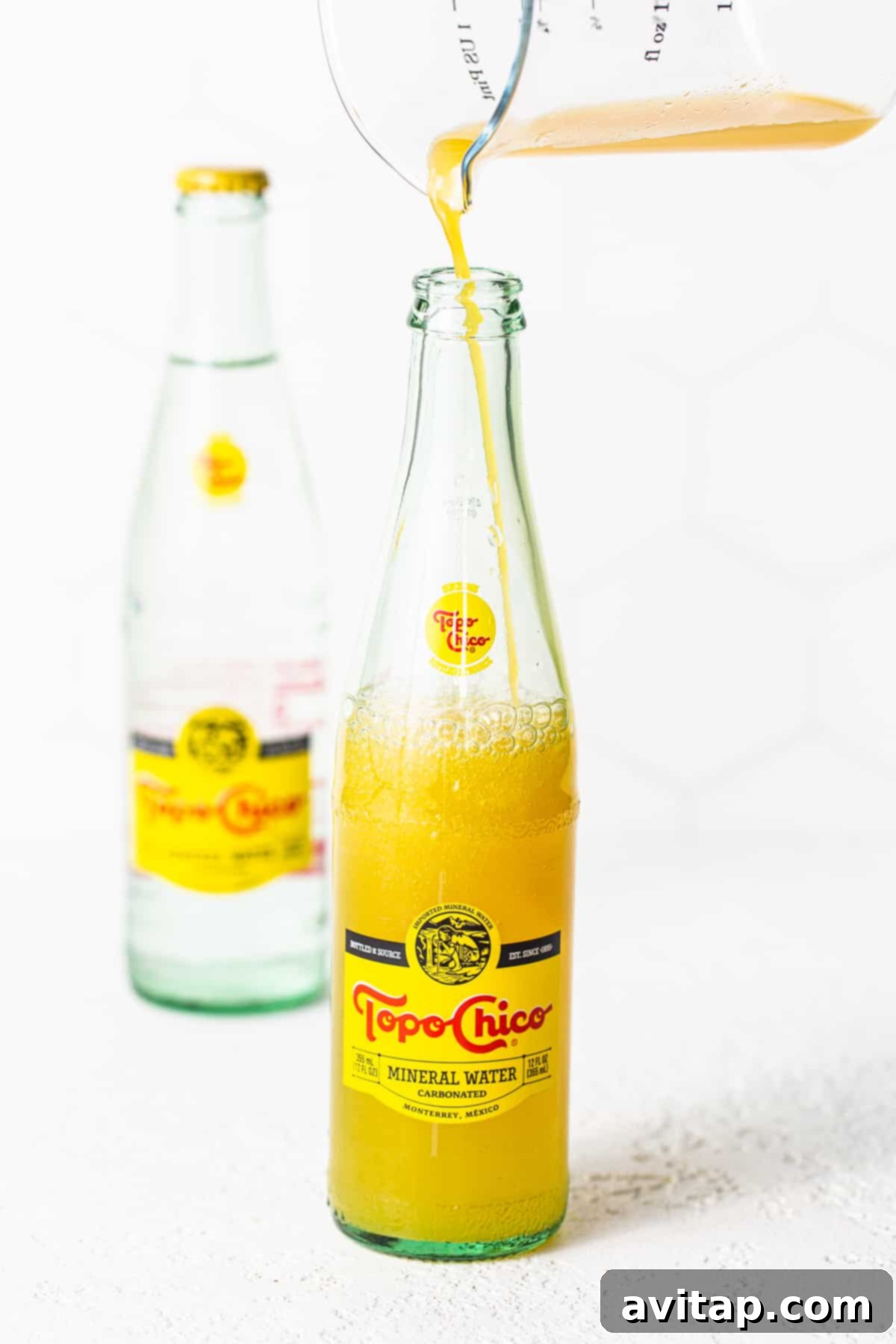 Mixing Ranch Water: Adding Juice to Topo Chico Mango juice being carefully poured into a Topo Chico bottle, ready to be mixed into Ranch Water.