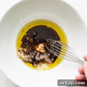 A person is whisking oil into a white bowl, preparing the marinade.