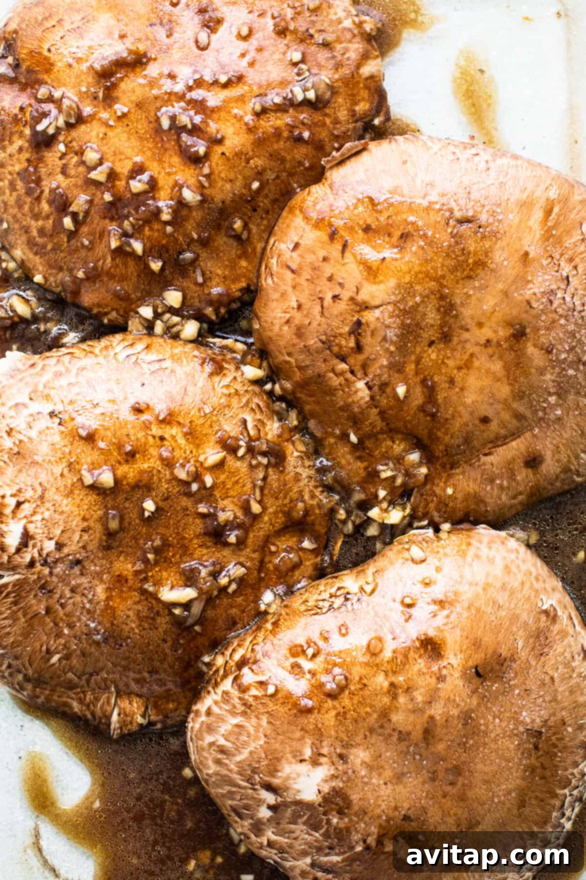 Portobello mushrooms generously coated in a dark, rich marinade, resting in a dish, anticipating the grill.