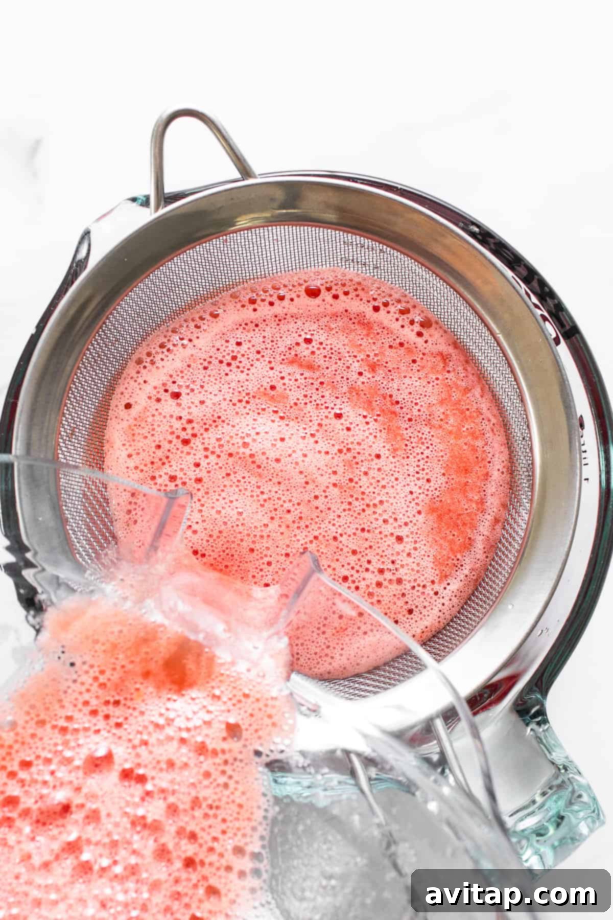 Sieving fresh watermelon juice through a fine-mesh strainer to achieve a smooth texture for wine freeze pops.