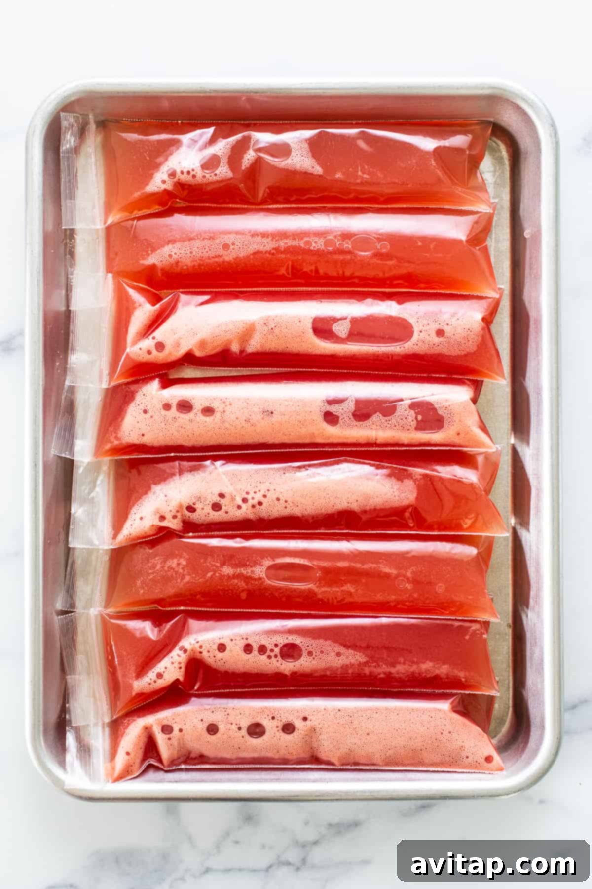 Watermelon wine freeze pops neatly arranged on a baking sheet, ready to be frozen solid.