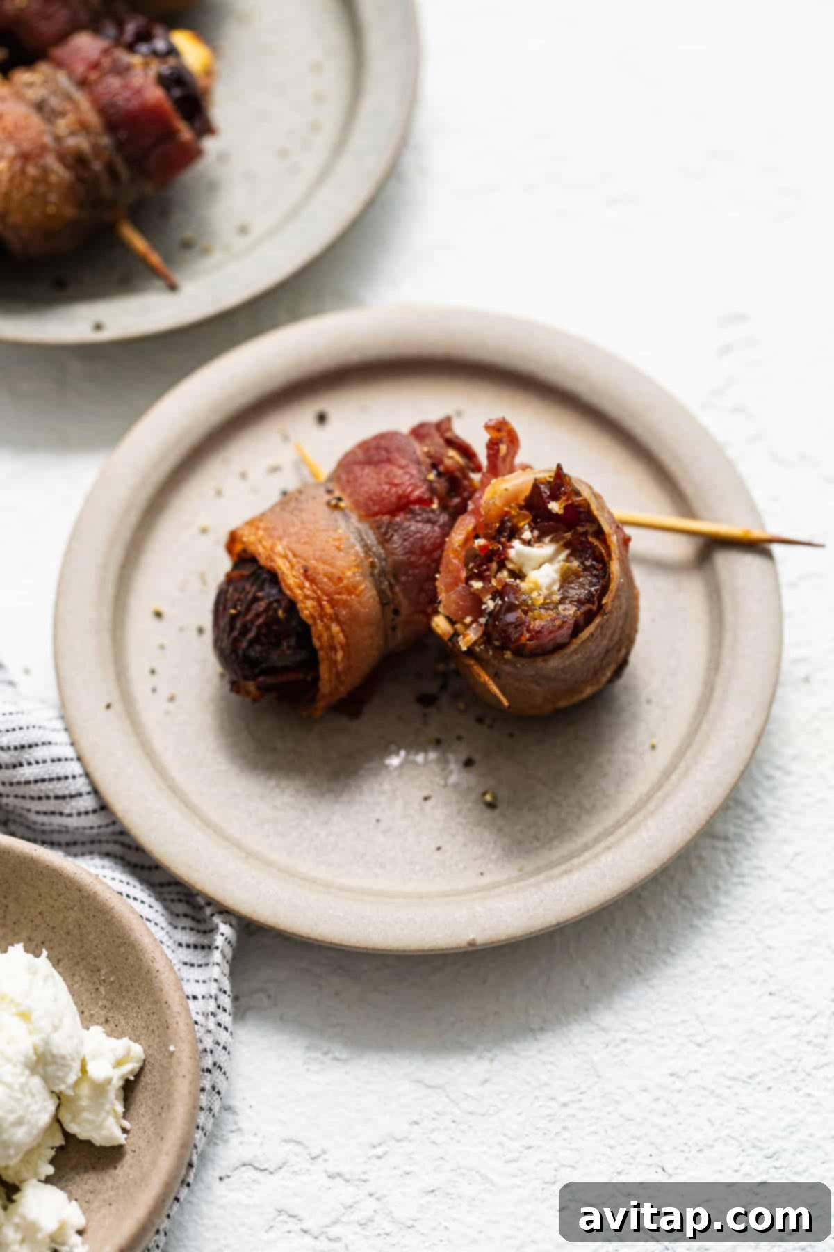 Bacon wrapped dates with goat cheese garnished on a plate.