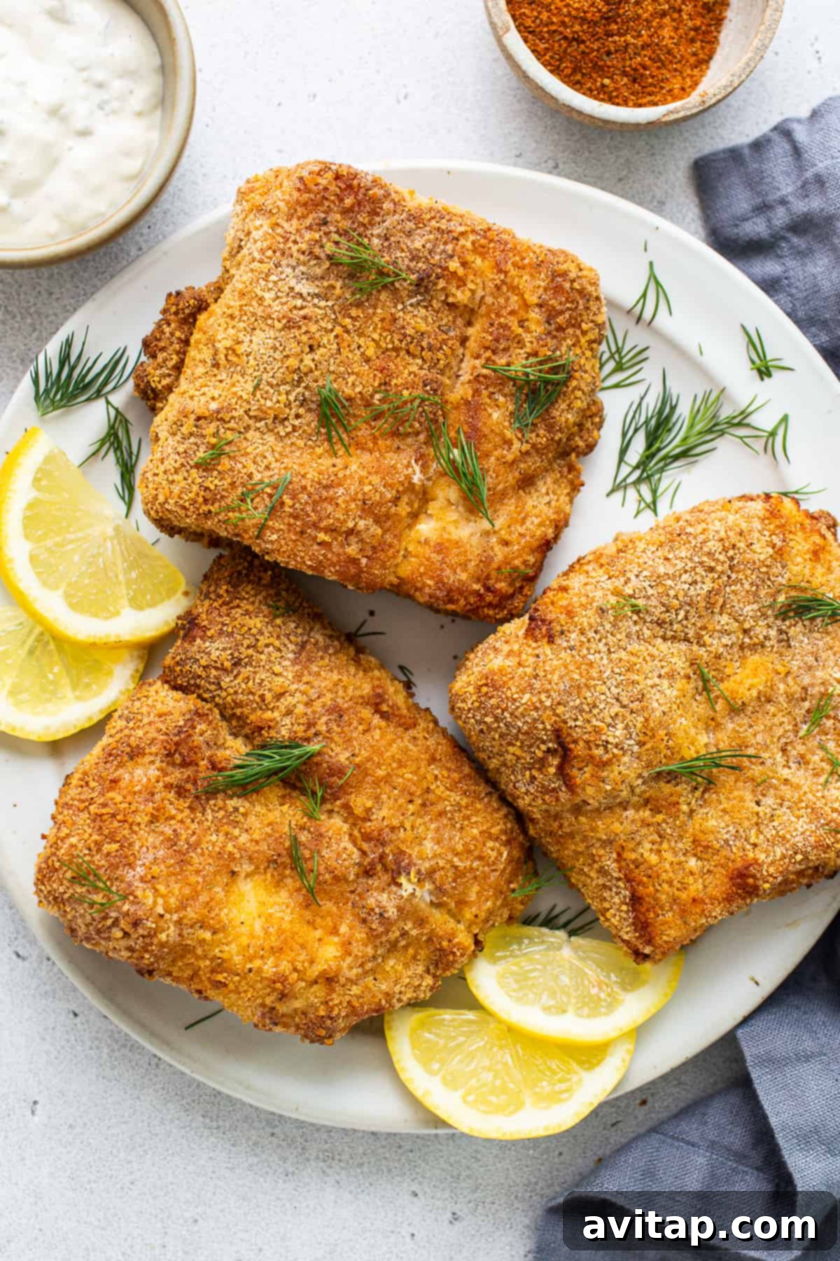 Air fryer fish on a plate with lemon slices.