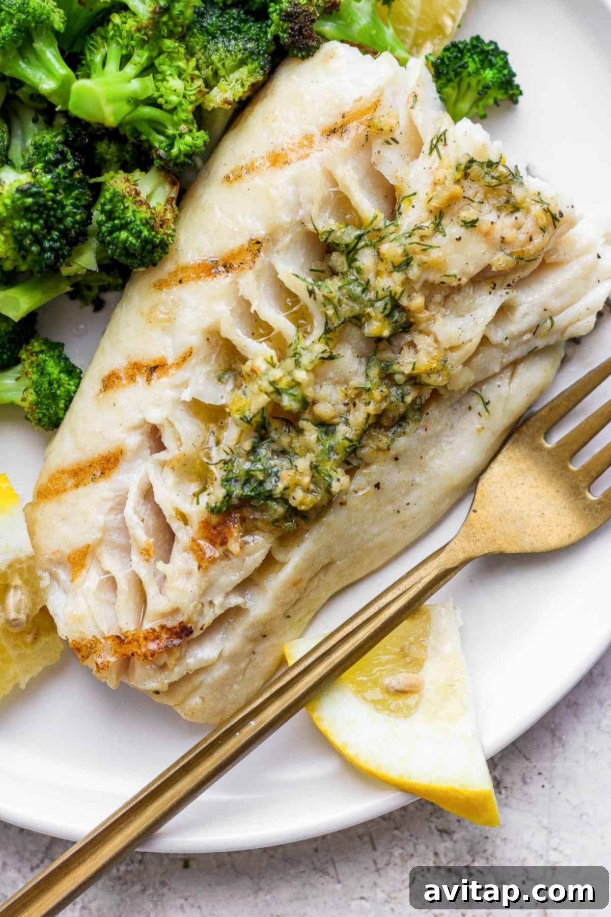 A serving of grilled fish on a plate, garnished with fresh herbs and served with a side of vibrant broccoli.