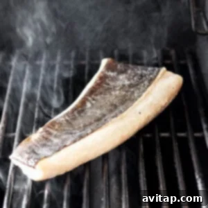 Filet of fish cooking on a hot grill with visible grill marks.