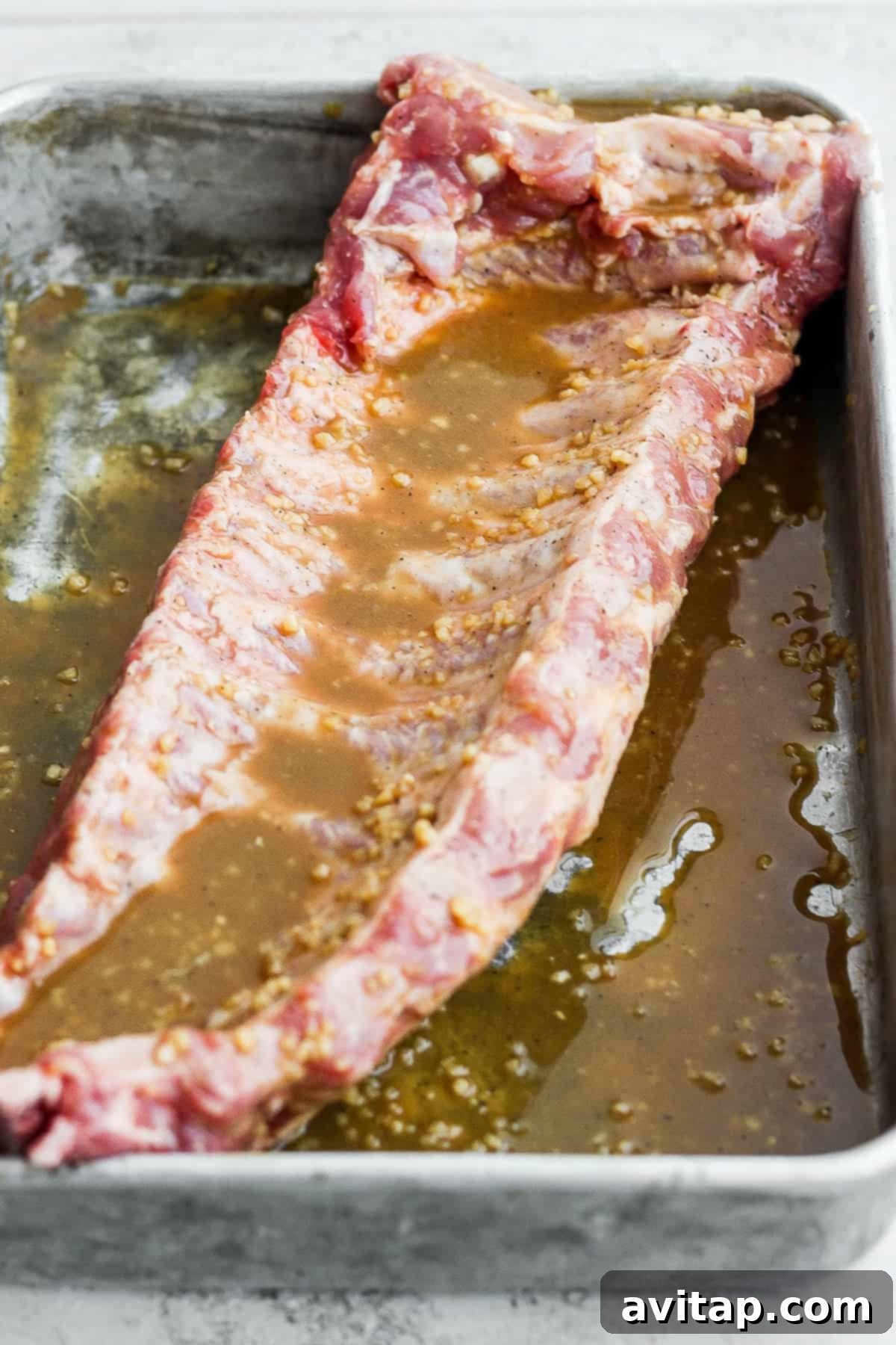 Rack of baby back ribs being marinated in a savory and sweet maple dijon sauce.