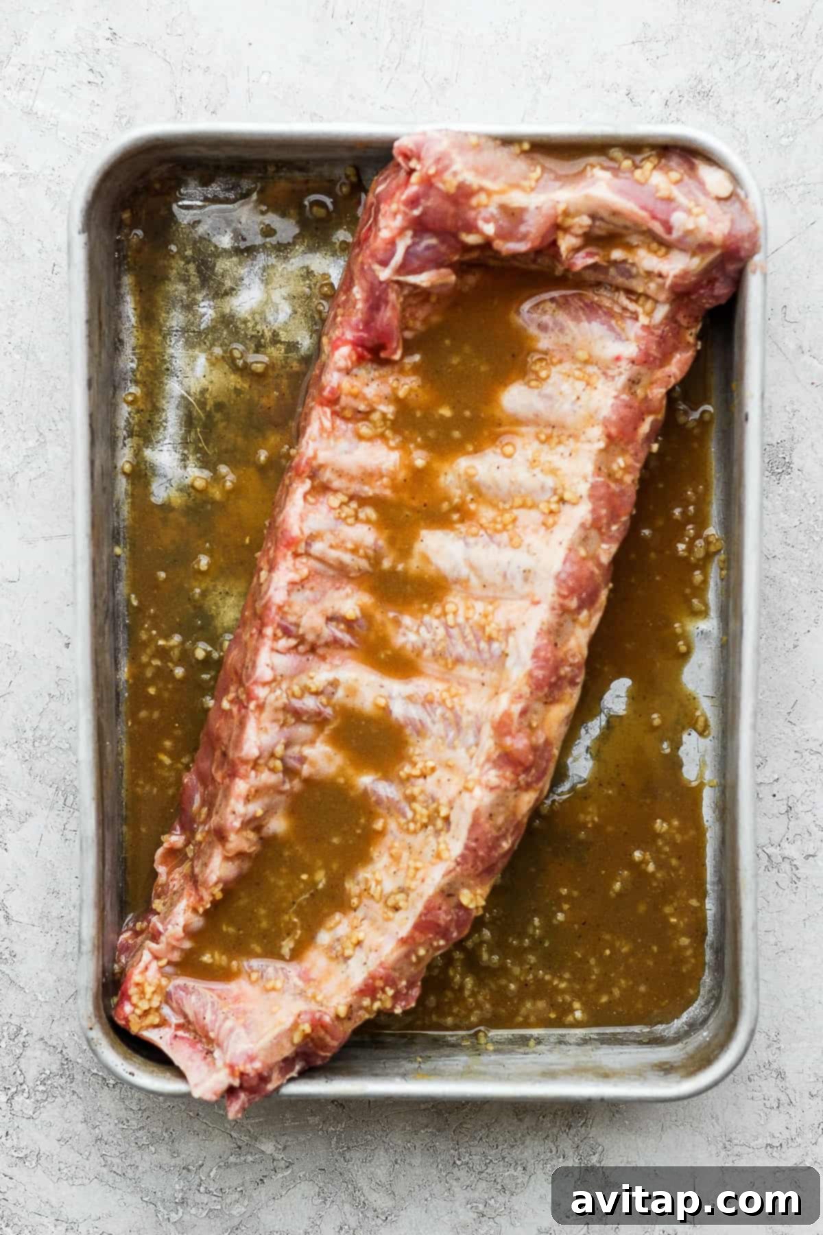A glistening rack of baby back ribs submerged in a rich maple dijon marinade, ready for cooking.