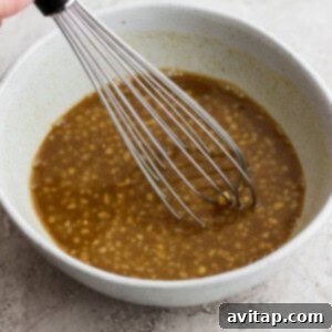 A hand whisking the maple dijon rib marinade in a bowl, showing a smooth brown liquid.