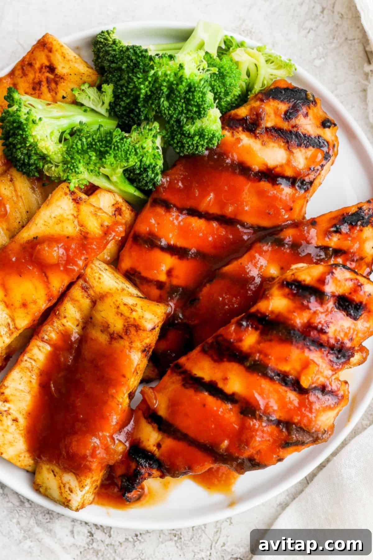A white plate topped with grilled pineapple chicken and fresh broccoli, showcasing a healthy and vibrant meal.