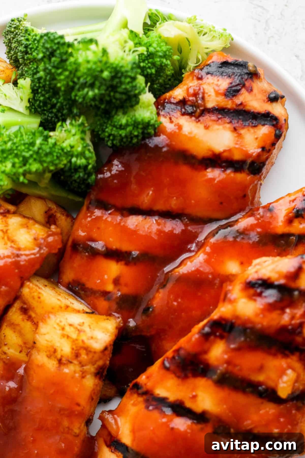 A serving of grilled pineapple chicken with broccoli on a white plate, highlighting a complete meal.
