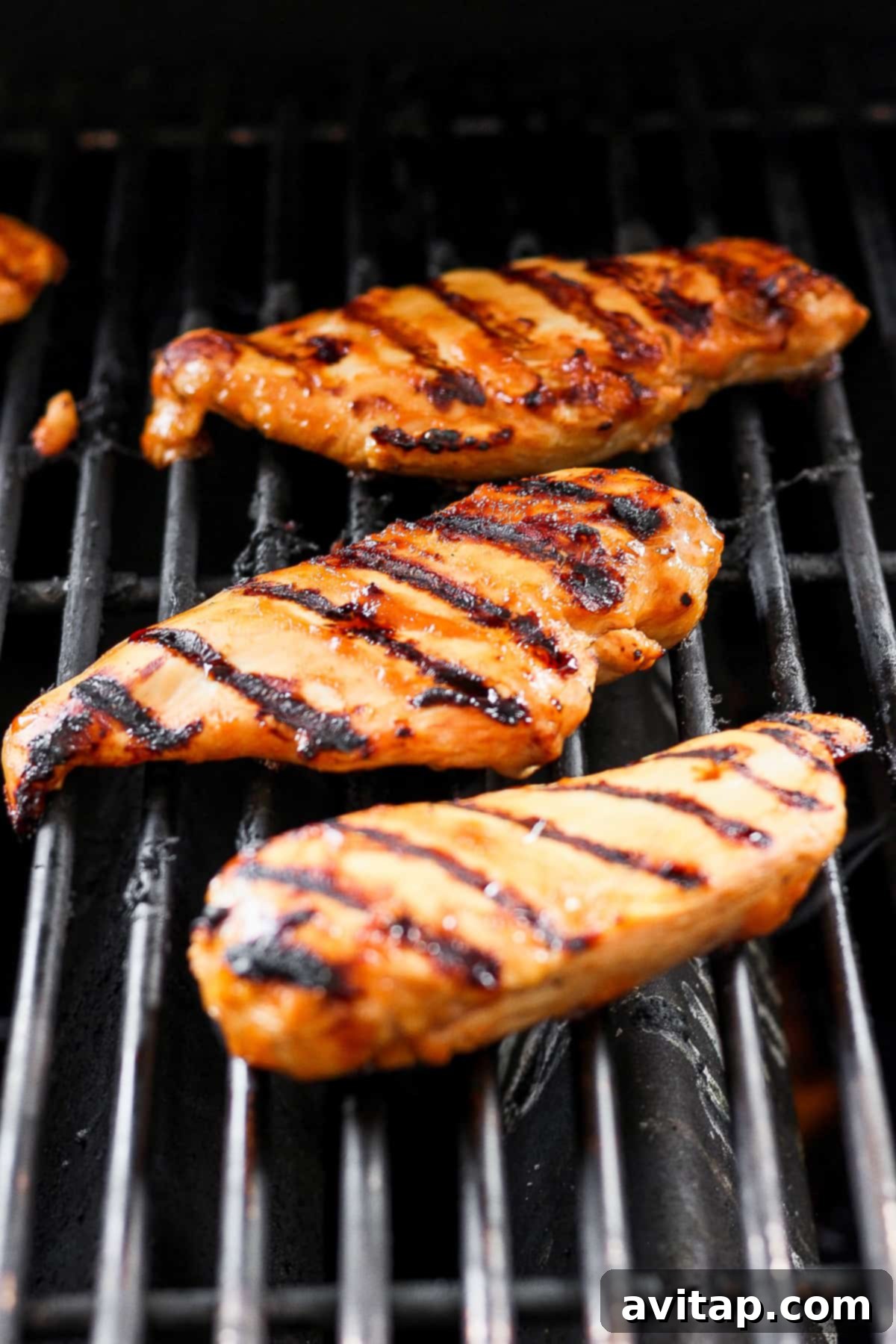 A close-up shot of grilled chicken breasts on a hot grill, showing sizzling and perfect charring.