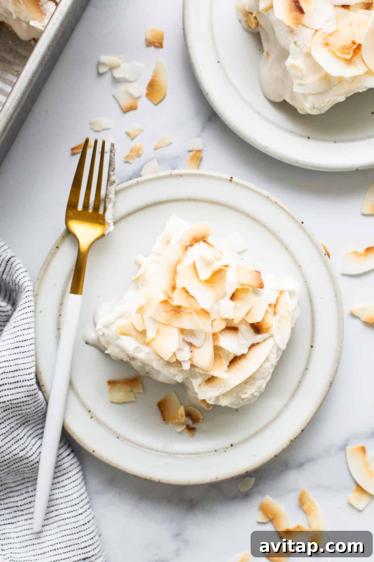 A single slice of coconut cream pie bar on a white plate, served with a fork, ready to be eaten.