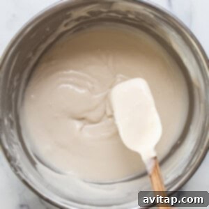 A hand holding a wooden spoon over a bowl of cream.