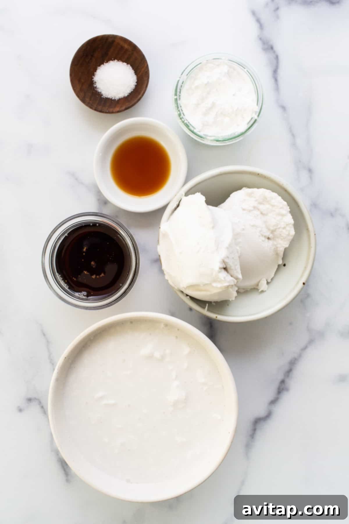 Various bowls of fresh ingredients including coconut flakes, heavy cream, and agave syrup, neatly arranged on a marble table, ready for baking.
