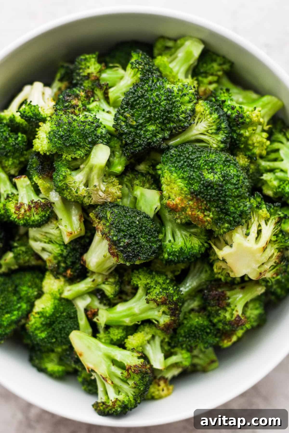 A white bowl filled with grilled broccoli on top of a rustic wooden table, garnished with fresh herbs.