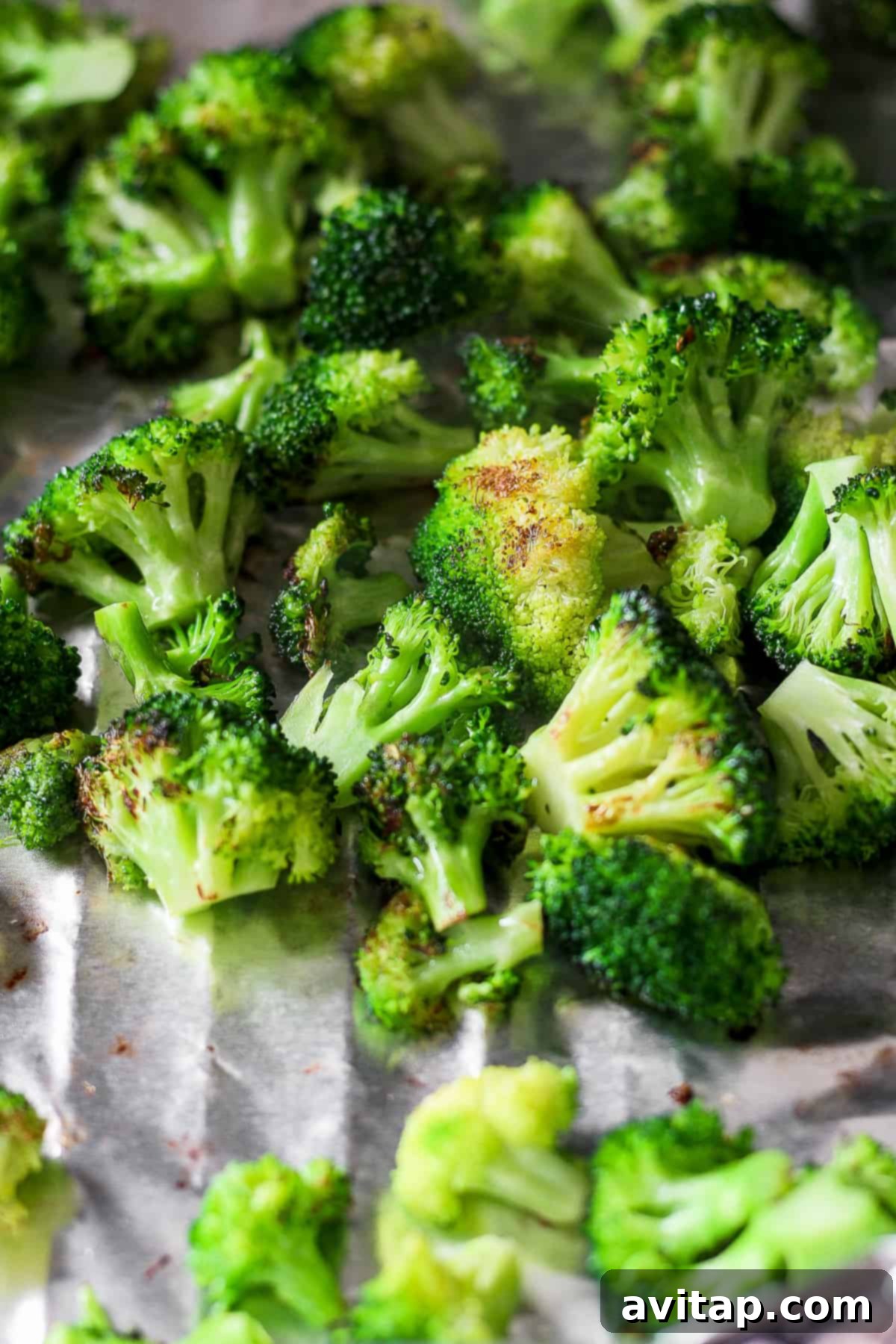 A bunch of raw broccoli florets seasoned and sitting on a sheet of foil, ready for grilling.