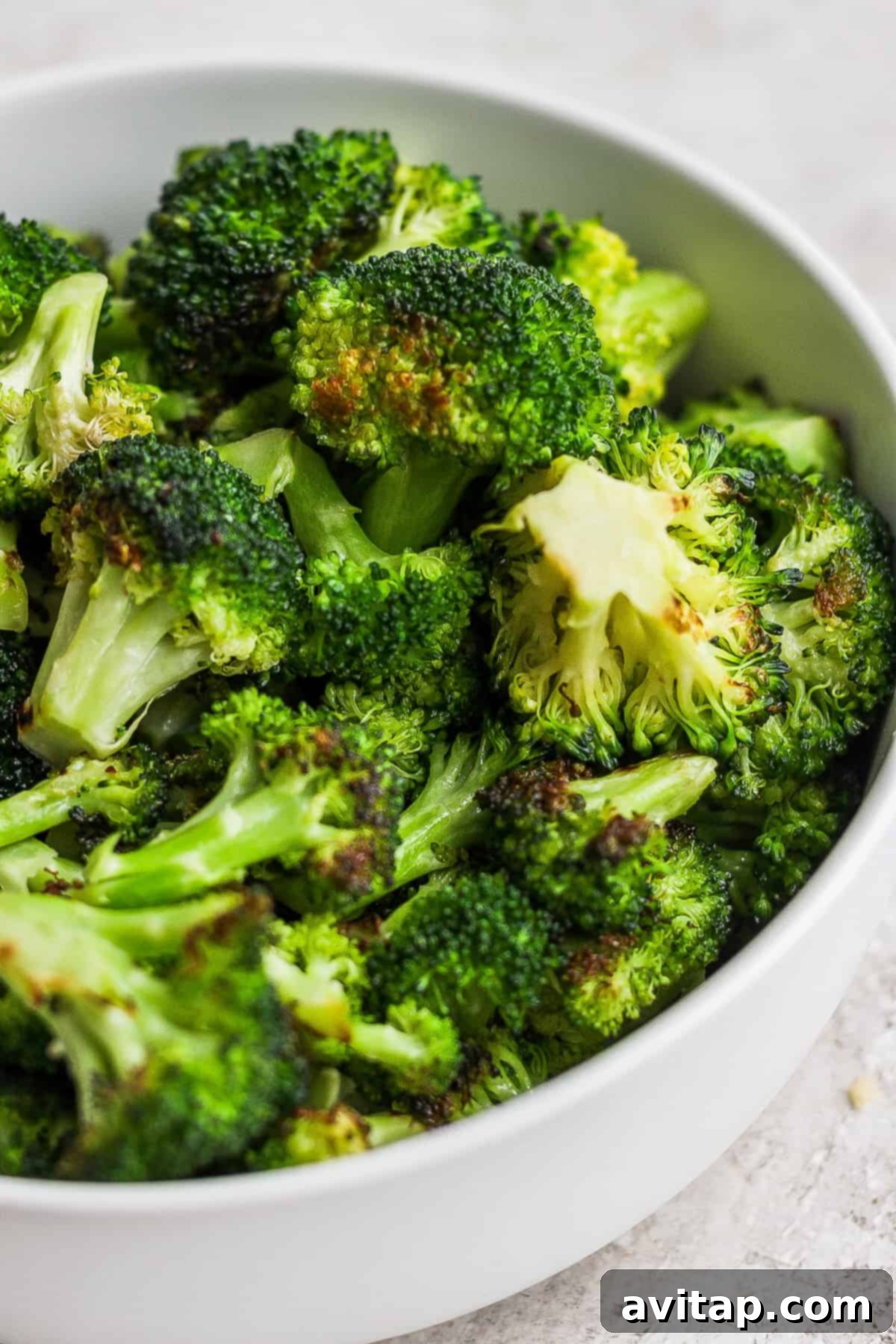 A white bowl filled with grilled broccoli on top of a table, showcasing the final dish.