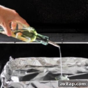 A person is pouring olive oil onto a grill covered with foil.
