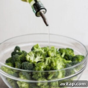 A bowl of broccoli with olive oil and seasonings, ready to be mixed.