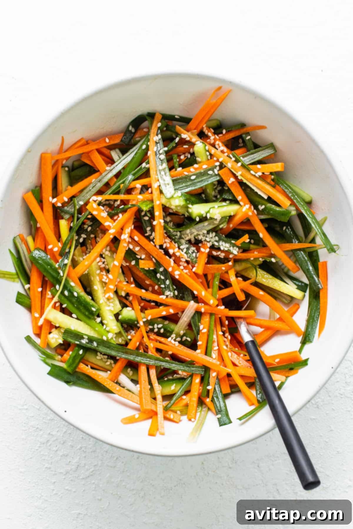 A crisp white bowl overflowing with freshly prepared matchstick carrots and vibrant green beans, ready for assembly.