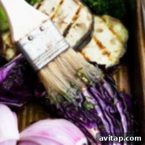 A close-up of a brush applying fresh herb dressing to grilled vegetables.