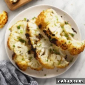 A white plate topped with grilled cauliflower next to a cutting board, garnished with fresh herbs.