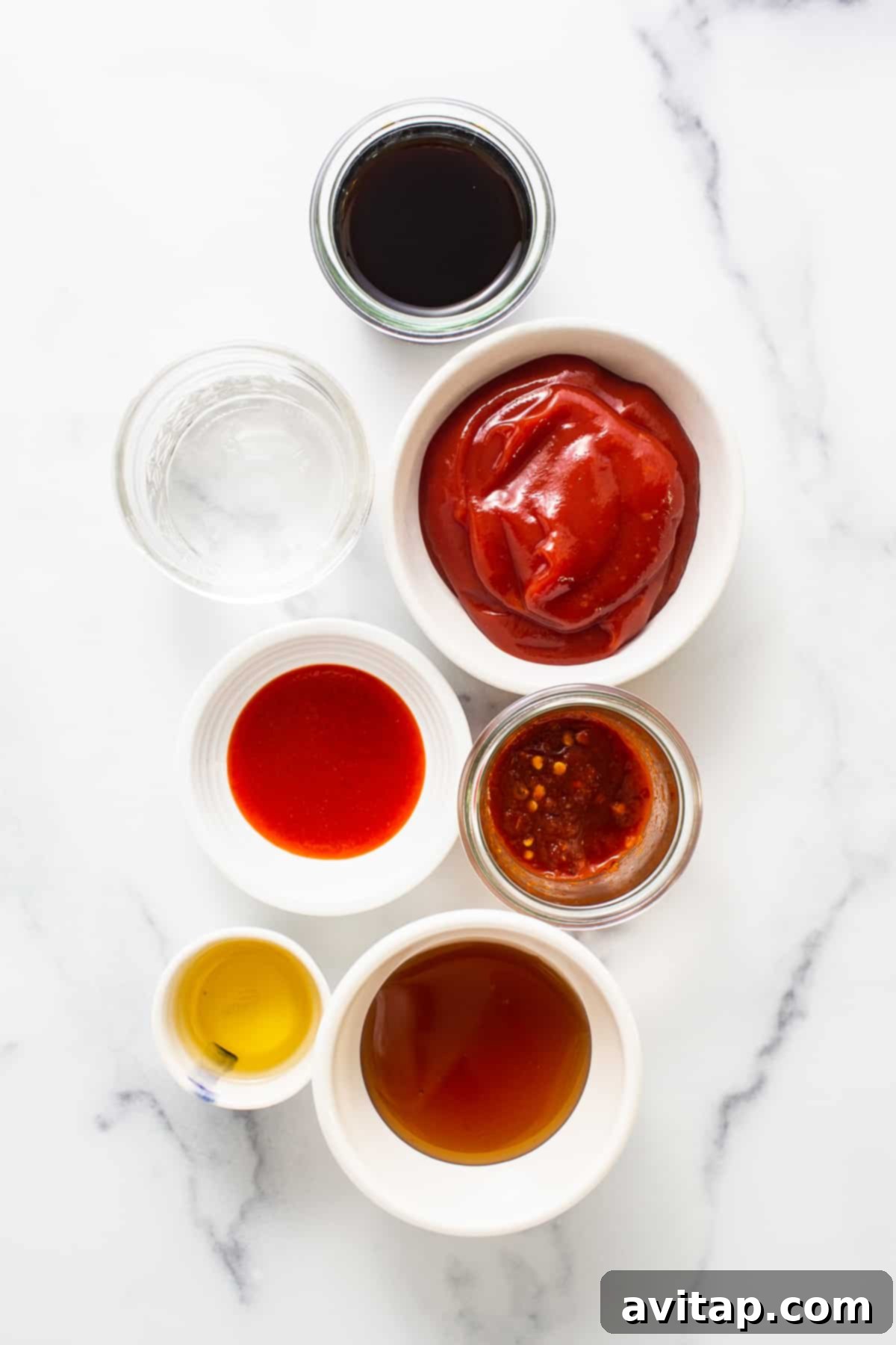 The seven essential ingredients laid out for a homemade firecracker sauce, featuring ketchup, honey, soy sauce, chili sauce, sriracha, water, and sesame oil.
