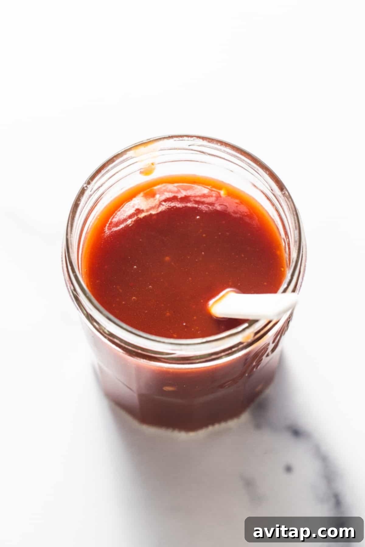 A sealed mason jar of homemade firecracker sauce with a spoon resting beside it, ready for storage.