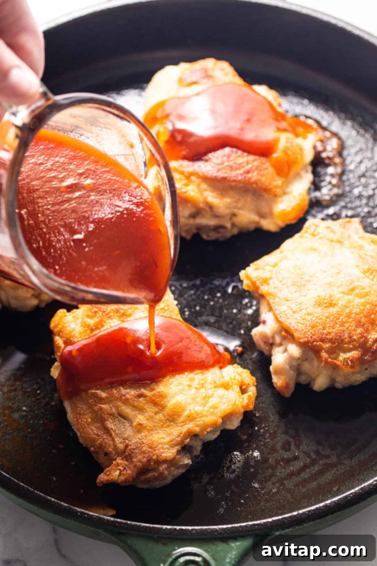A person adding ketchup to a dish in a skillet, showcasing the cooking process.