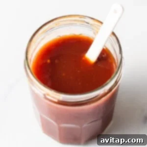 homemade firecracker sauce in a jar with a spoon, showing its vibrant color and smooth texture.