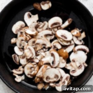 Effortless Sautéed Mushrooms 10 Mushrooms sautéing in a skillet on a white background.