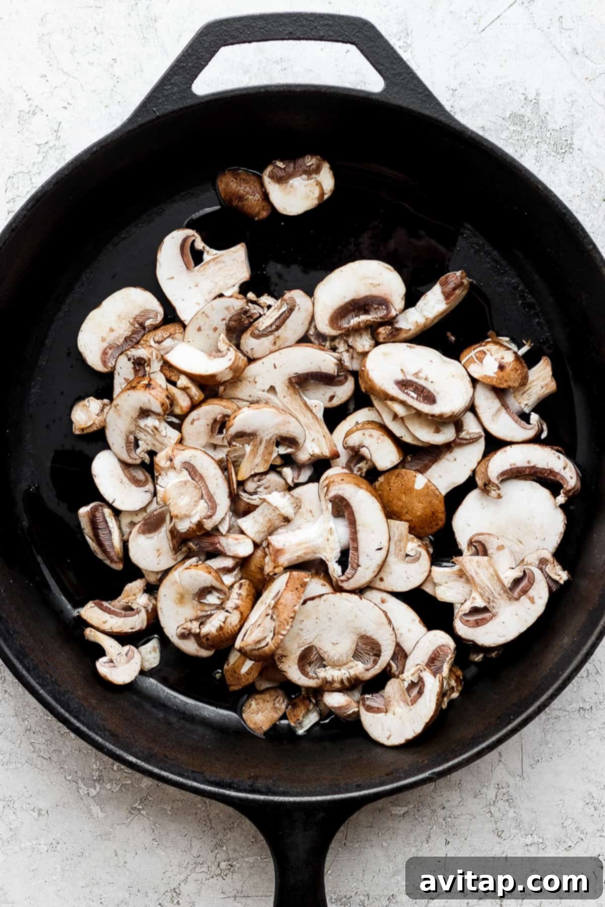 Effortless Sautéed Mushrooms 6 Sautéed mushrooms glistening in a skillet on a clean white background, highlighting their readiness and appealing texture.