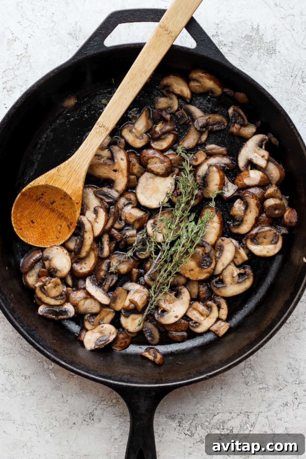 Effortless Sautéed Mushrooms 7 Golden-brown sautéed mushrooms in a skillet with a wooden spoon, ready to be served or incorporated into a dish.